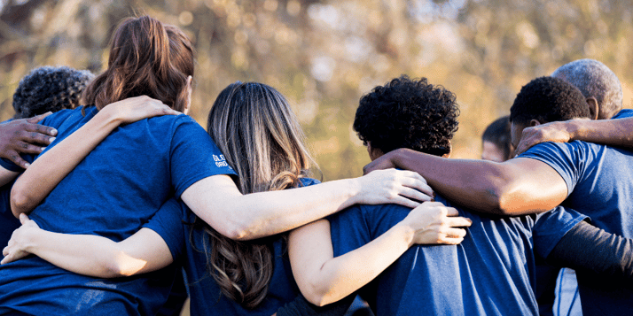 Several people with arms around each other and backs turned to the camera. 